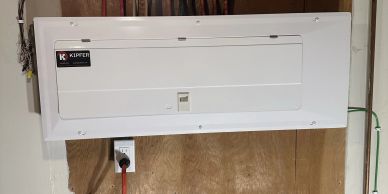 Electrical breaker panel mounted on wooden wall above outlet.