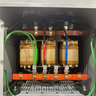 Three-phase transformer with colored wiring inside a control panel.