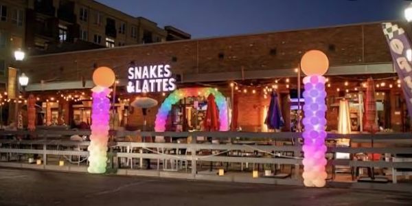 Night view of Snakes &amp; Lattes cafe with colorful balloon columns outdoors.