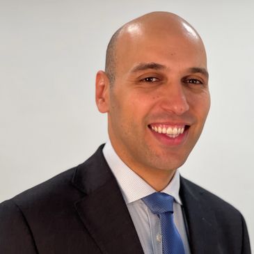 Smiling bald man in a suit and blue tie against a plain background.