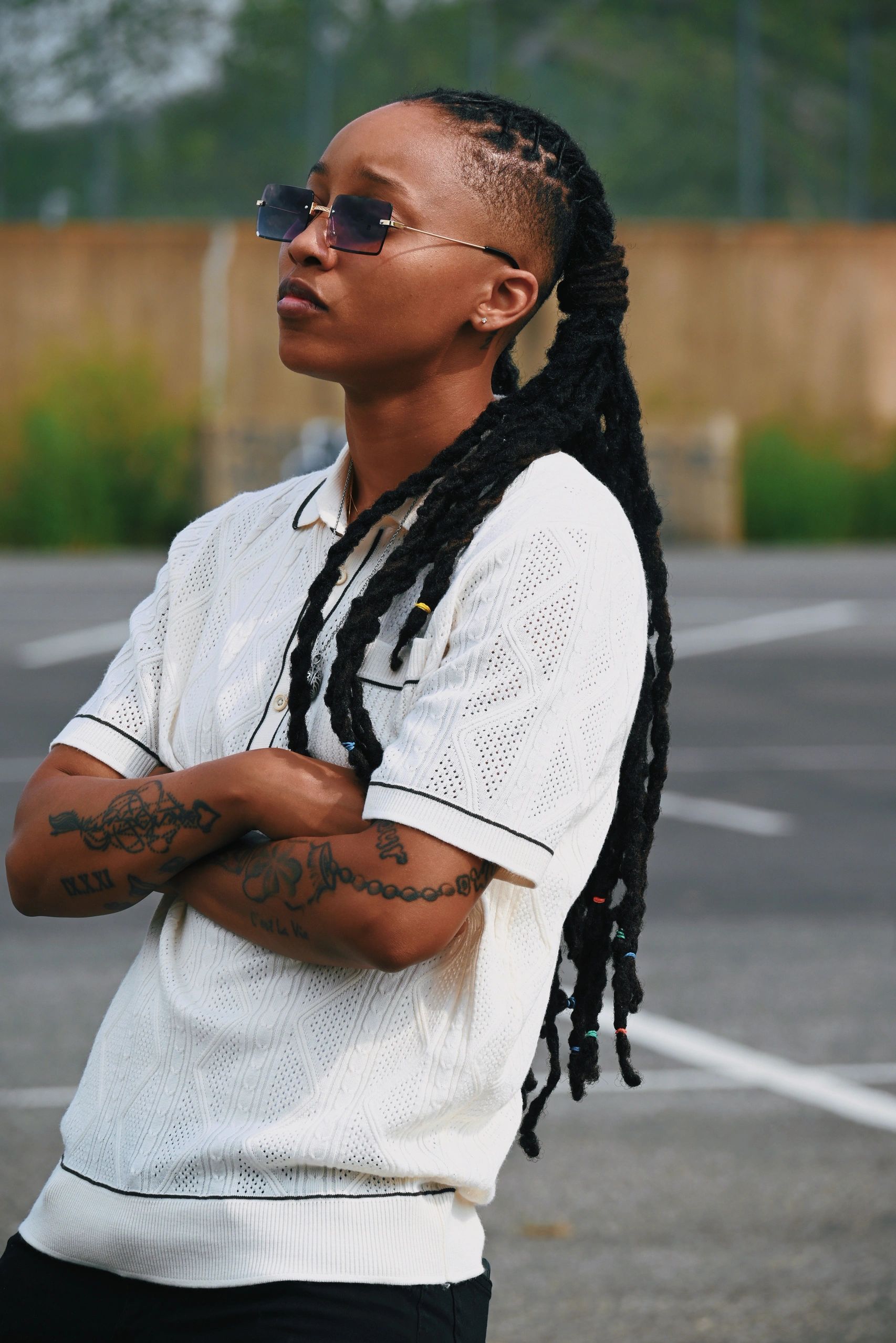 Person with long dreadlocks and sunglasses looking thoughtfully.