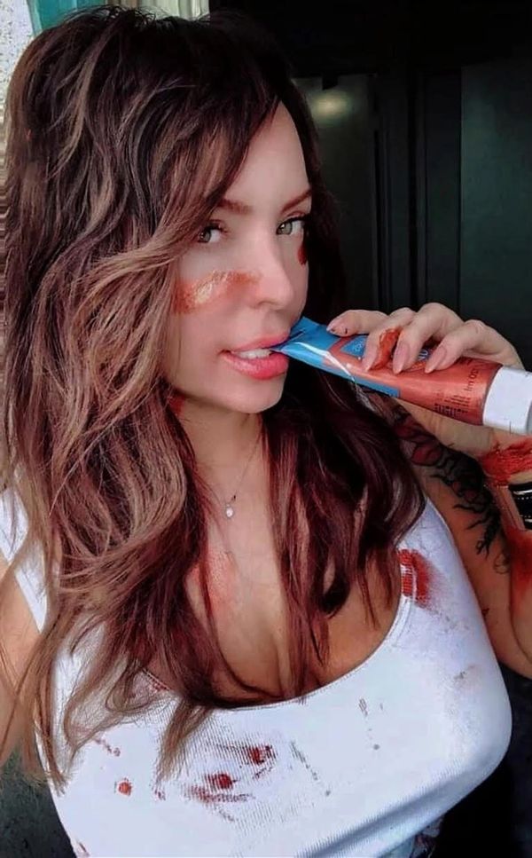 Woman with paint smudges on her face and shirt, holding a paint tube near her mouth.