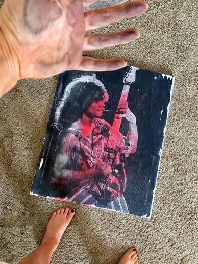 A hand and feet near a worn guitar player poster on carpet.