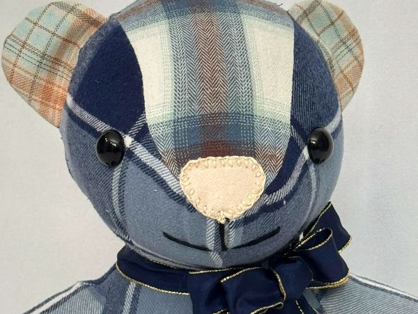 Close-up of a blue plaid stuffed bear with a navy blue bow.