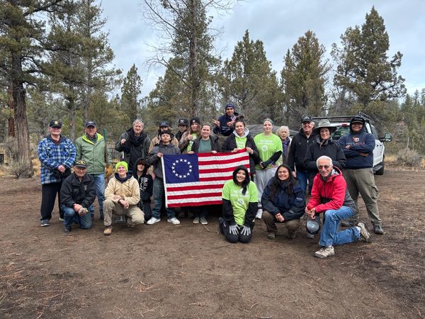 Group of people outdoors holding a Betsy Ross flag in a forested area.