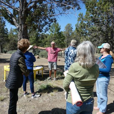 Man in pink shirt speaks to a group outdoors under clear skies.