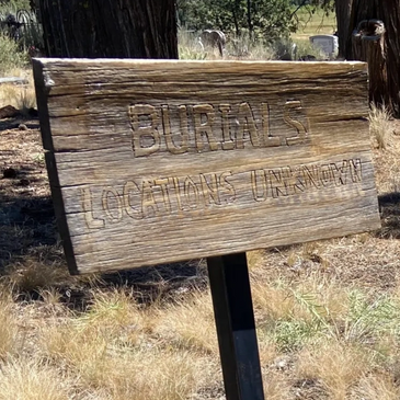Wooden sign in a dry grassy cemetery area.