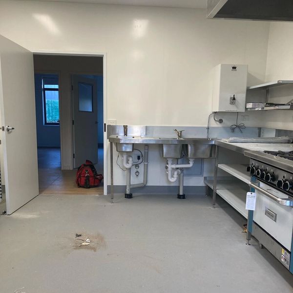 Empty commercial kitchen space with stainless steel sinks and stove.