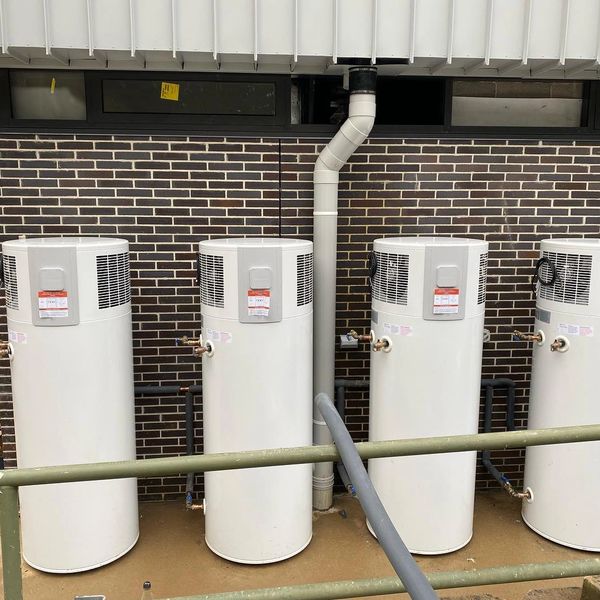 Four white water heaters installed outdoors.