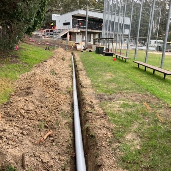Long pipe laid in a trench near a sports field.