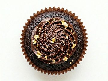 A chocolate cupcake with rich frosting and gold leaf decoration.