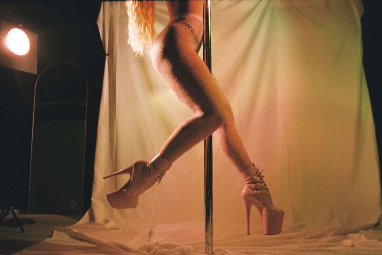 A person pole dancing with pink high heels and fishnet stockings.