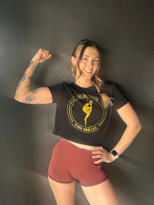 Smiling woman flexing her arm, wearing a black crop top and red shorts.