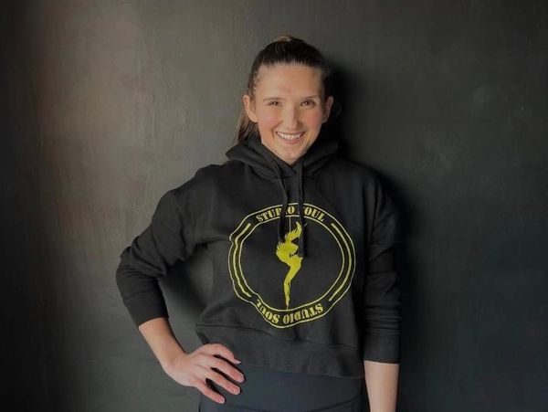Smiling woman in black hoodie posing against a dark wall.