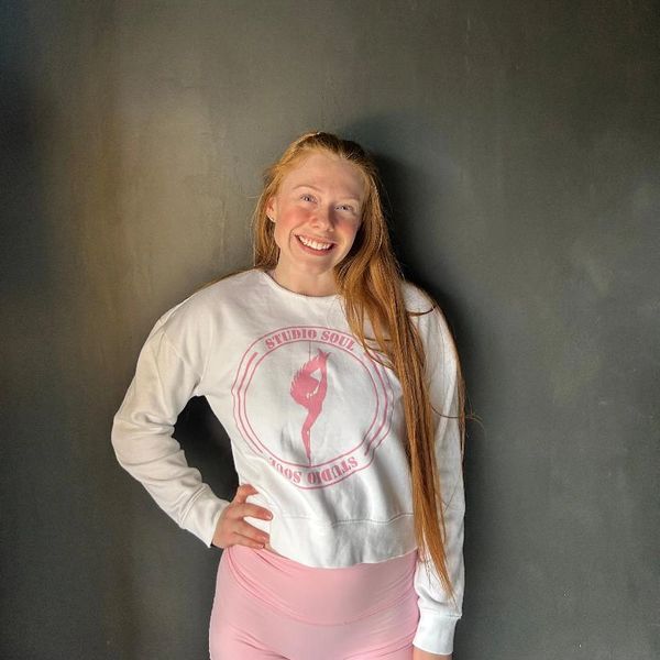 Smiling young woman with long red hair in white sweatshirt and pink leggings.