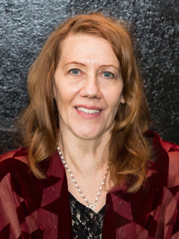Smiling middle-aged woman with red hair and pearl necklace against a black background.