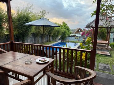 Cozy outdoor seating area overlooking a pool and garden with umbrella and greenery.