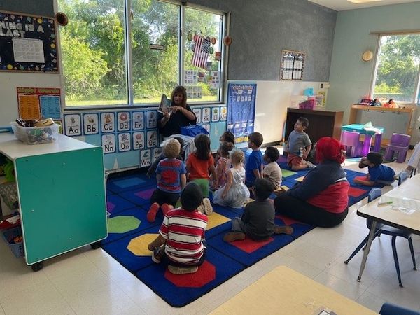 Teacher reading a book to young children sitting on a colorful classroom rug.