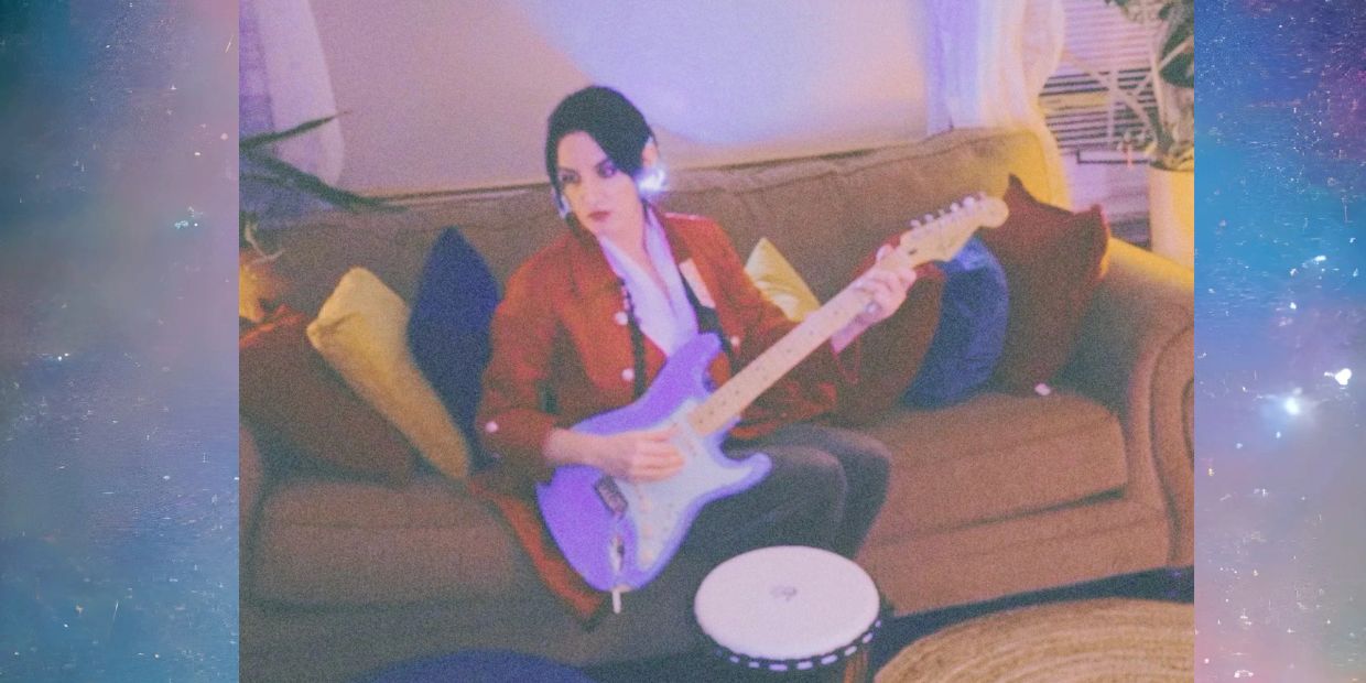 Person playing electric guitar on couch.