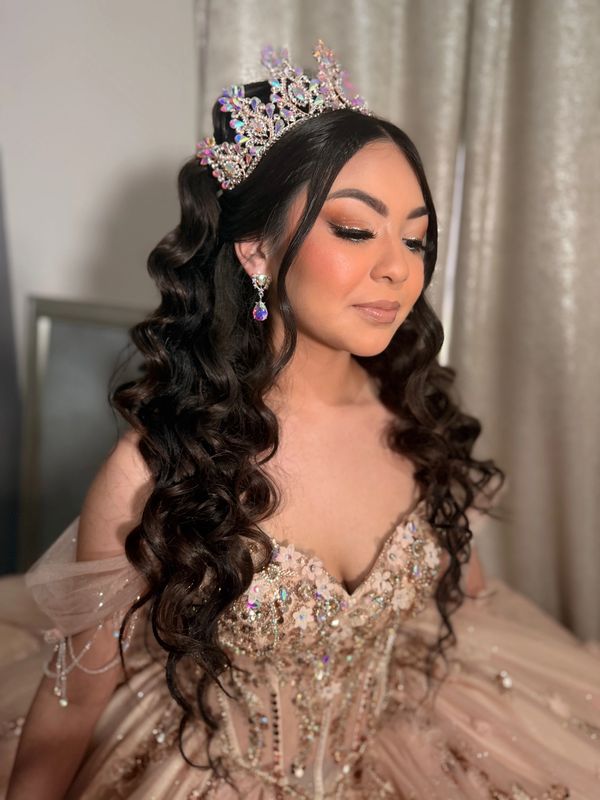 Young woman in a jeweled crown and elaborate dress poses gracefully.