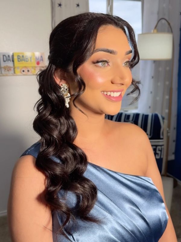 Woman with glossy curled hair wearing a shiny blue off-shoulder dress and elegant earrings.