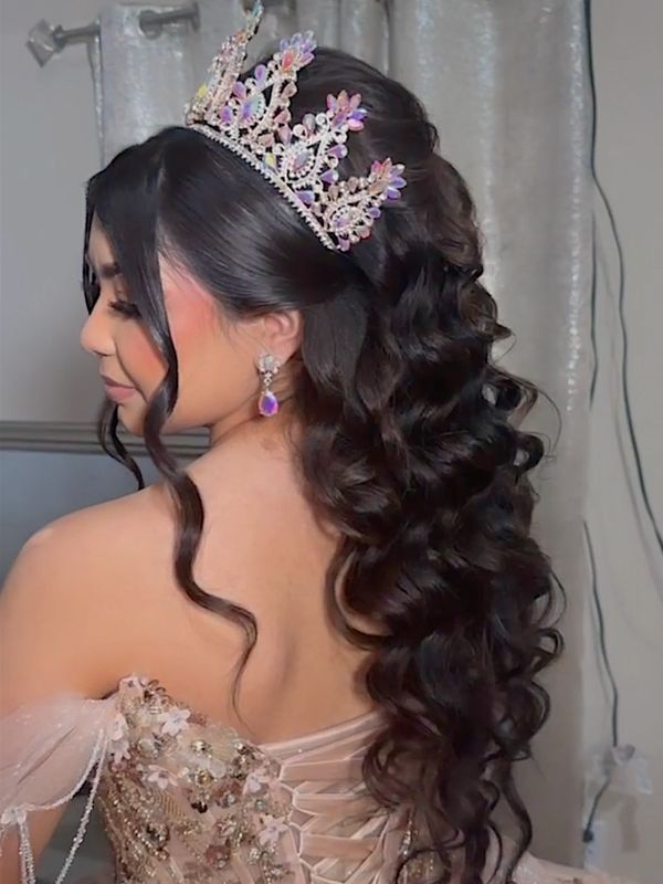 Woman with long curly hair wearing a jeweled crown and elegant dress.