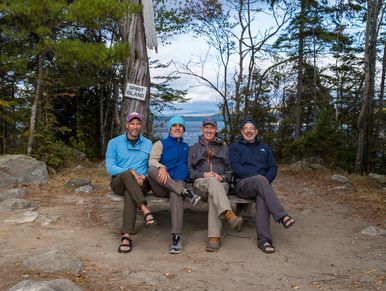 Four men sitting on a bench at Spirit Bald with a scenic forest view.