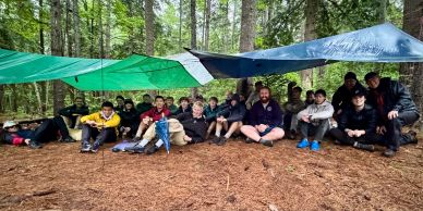A group of people sitting under tarps in a forest setting.