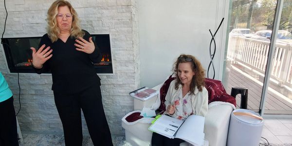 Two women engaged in a discussion in a cozy, well-lit room with a fireplace.