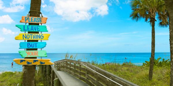 Colorful sign by the beach with a wooden pathway and ocean view.