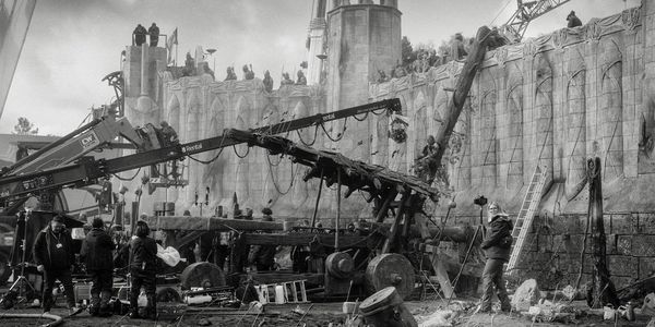 Black-and-white photo of a film crew shooting a medieval battle scene with castle walls.