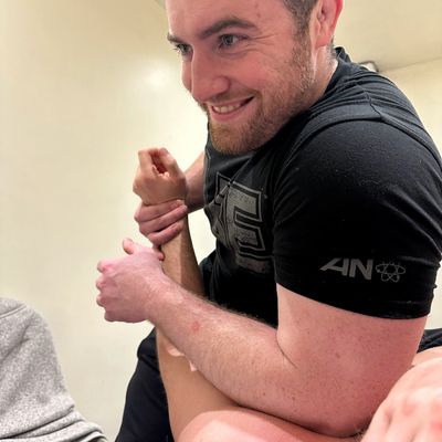 Man smiling while adjusting another person's arm, possibly during therapy or training.