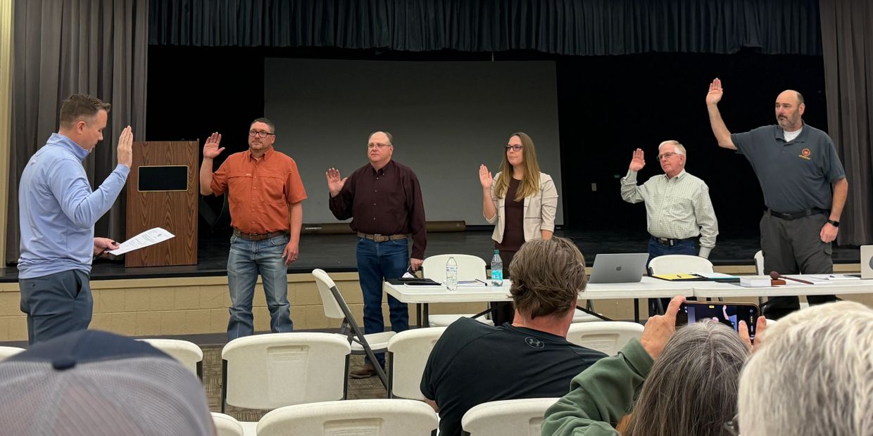 Six people raise their right hands during a formal swearing-in ceremony inside a hall.
