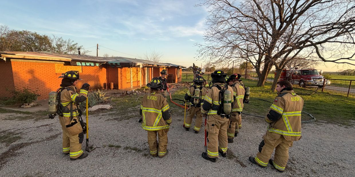 Firefighters in gear gather outside a building during sunset.