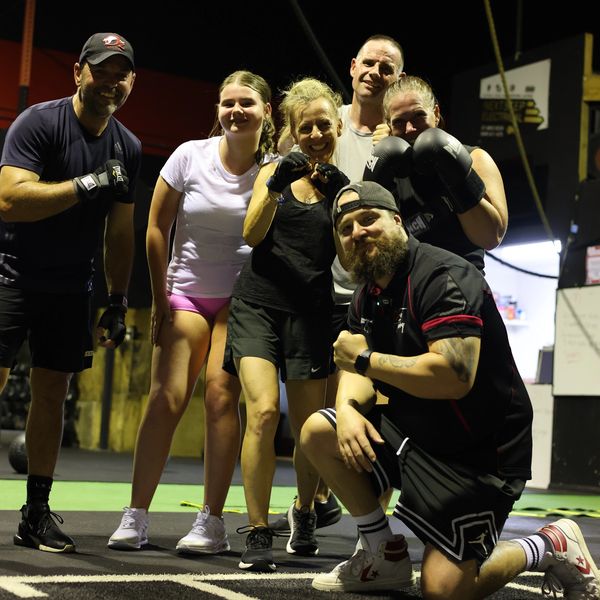 Group of people posing in a gym with boxing gloves and athletic wear.