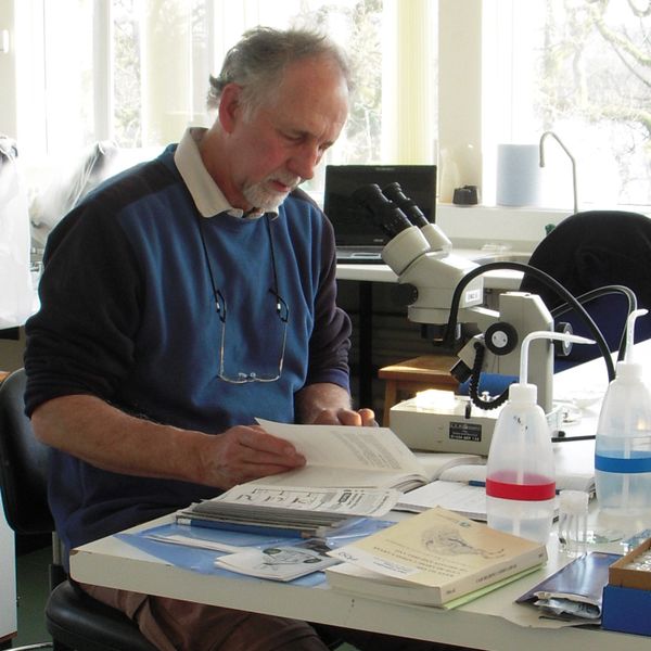 A man reading a book next to a microscope in a well-lit room.