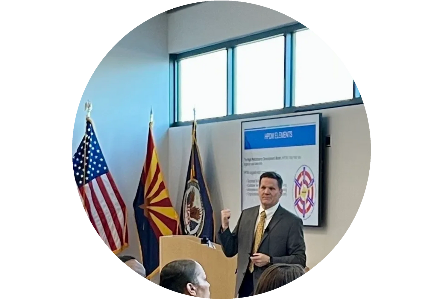 Man in suit giving a presentation with flags and a screen behind him.