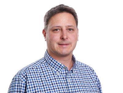Man in a blue checkered shirt smiling against a white background.