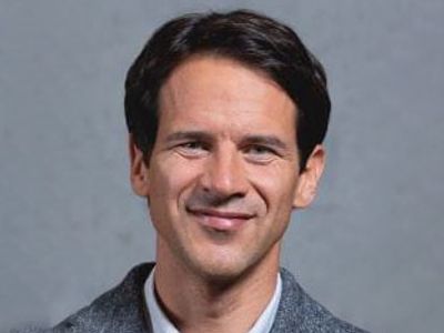 Portrait of a smiling man with dark hair against a gray background.