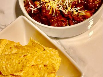 Bowl of chili topped with shredded cheese and a plate of tortilla chips.