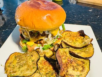 Juicy cheeseburger with grilled eggplant slices on a white plate.