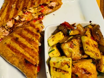 Grilled chicken wrap with sautéed vegetables on a white plate.