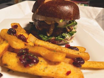 Gourmet burger with fresh greens and thick fries topped with dried cranberries.