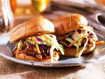 Two pulled pork sandwiches with coleslaw on a metal plate.