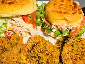 Two turkey sandwiches with lettuce, tomato, and fried green tomatoes on the side.