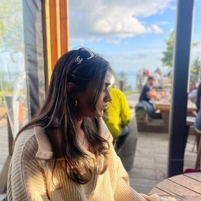 Young woman in cozy sweater sitting at outdoor café, lost in thought.