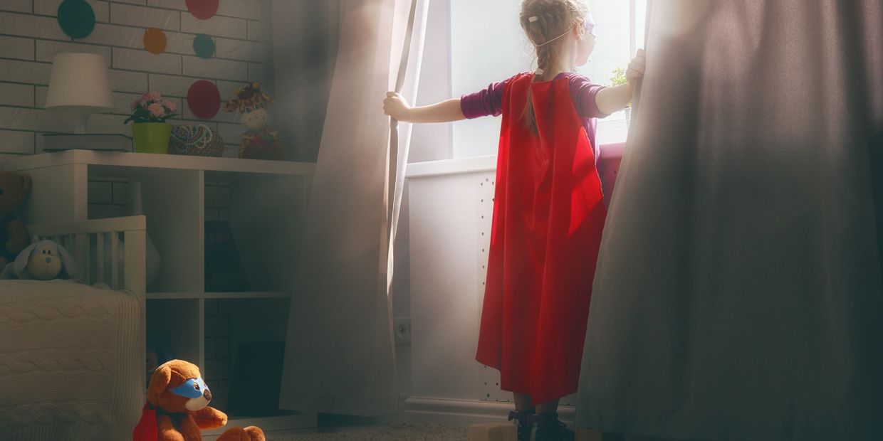 picture of a child wearing a superhero costume looking out a window.