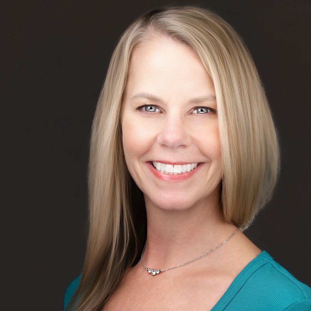 Smiling woman with blonde hair against a dark background.