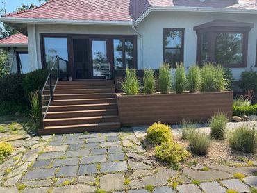 Modern house entrance with wooden steps and greenery.