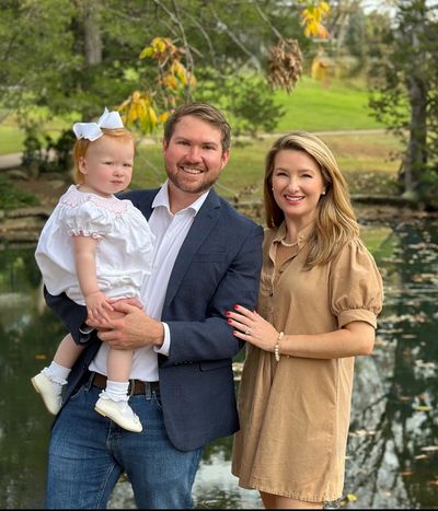Family of three posing outdoors by a pond.
